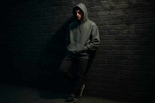 Young man in an oversized winter hoodie with jogger pants, leaning against a brick wall, moody winter streetwear vibe, cinematic lighting.